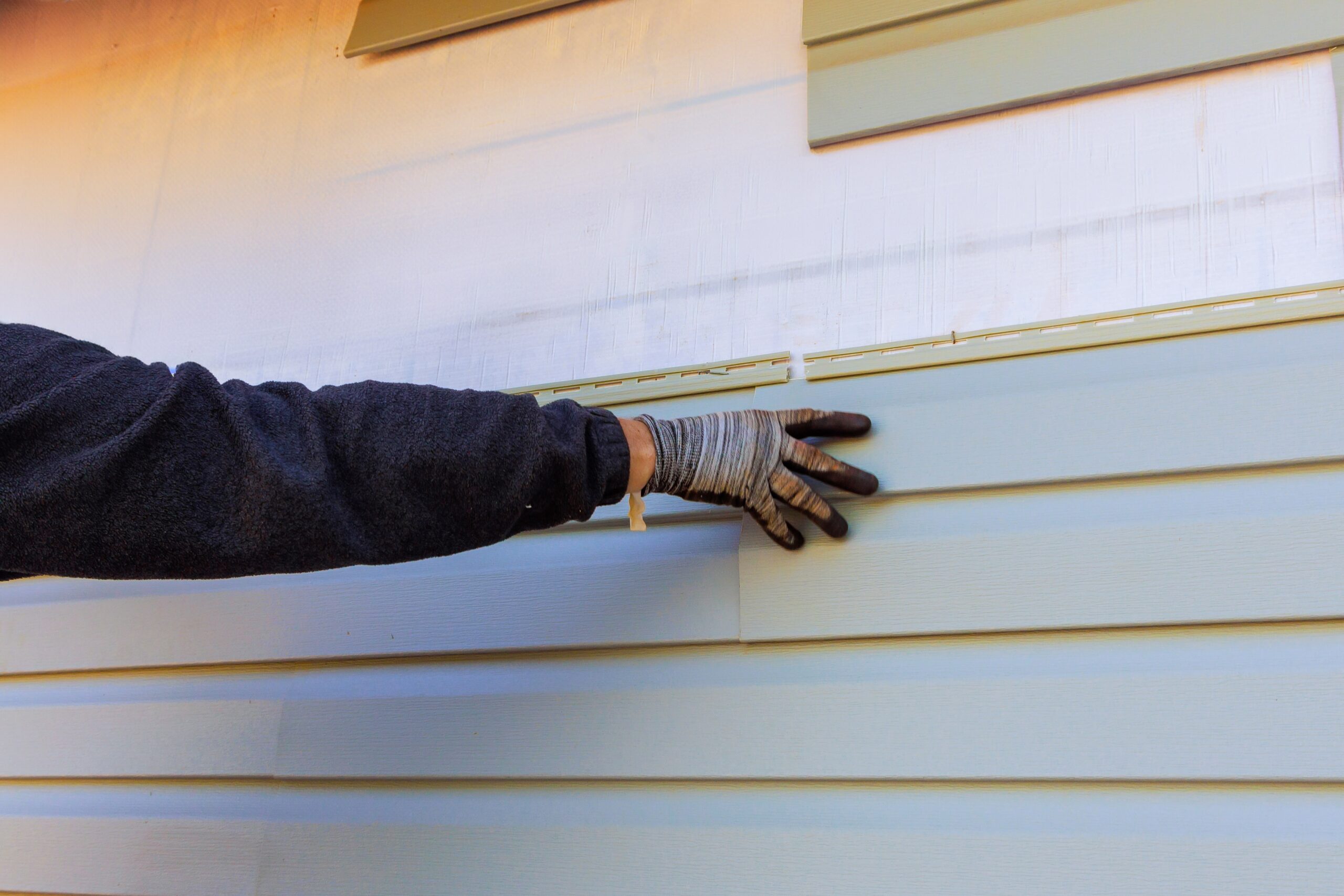Roof Hounds technician installing vinyl siding on a home in Utah, demonstrating expert siding installation services for improved curb appeal and protection.